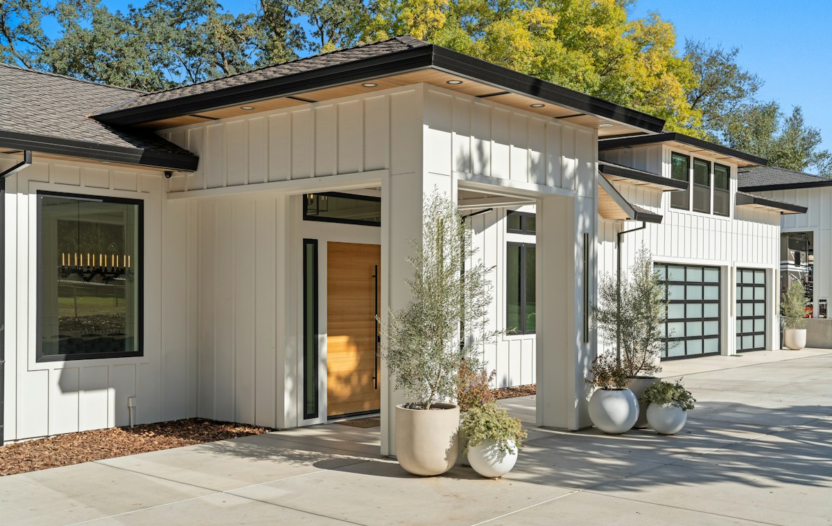Modern white farmhouse with black trim, glass garage doors and landscaped garden